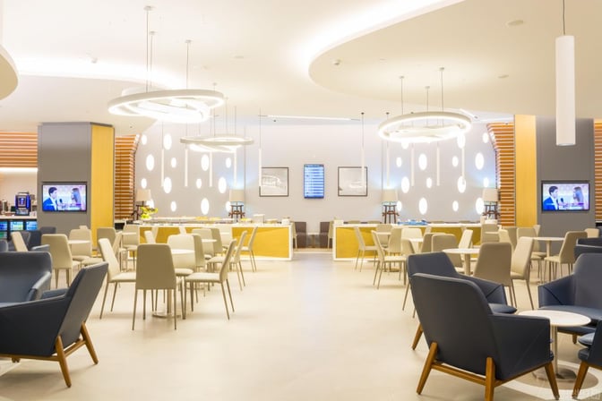 The Ahlein Premium Lounge at Beirut Airport features a seating area with tables, chairs, and a self-serve food station.