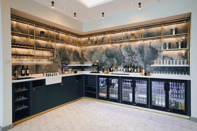 The Aspire Lounge at Belfast City Airport features a bar area with a selection of spirits, wines, and refrigerated beverages.