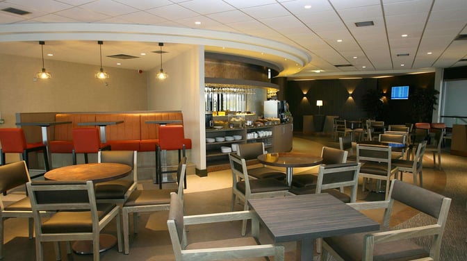 The Causeway Lounge at Belfast International Airport features a seating area with tables and chairs, adjacent to a self-serve food station.