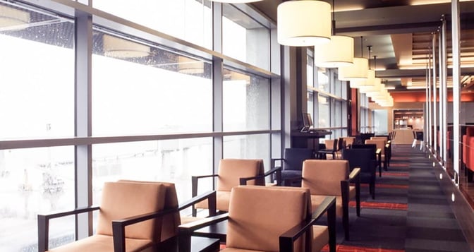 Seating area in Dan Lounge at Ben Gurion Airport features armchairs along large windows with views of the tarmac.