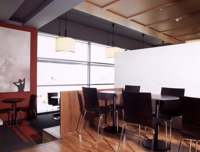 Seating area in Dan Lounge at Ben Gurion Airport features round tables and chairs with views of the airport through large windows.