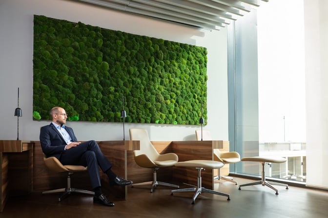 The seating area in Lounge Tegel at Berlin Brandenburg Airport features individual workstations with chairs, lamps, and a large green wall.