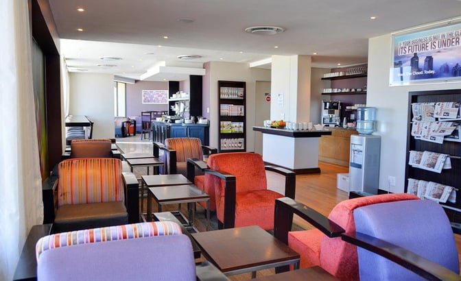 The Bidvest Premier Lounge at George Airport features comfortable seating, a self-serve beverage station, and a selection of newspapers.