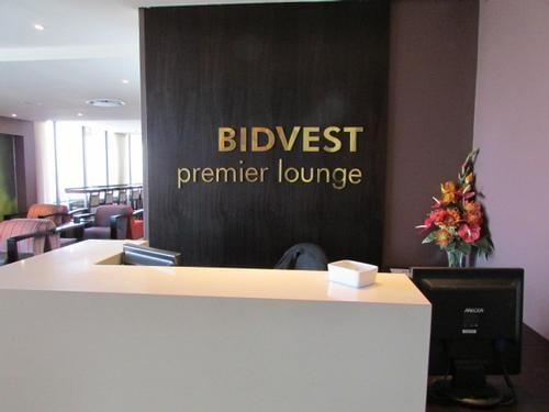 The Bidvest Premier Lounge entrance at George Airport features a reception desk with a computer and floral arrangement.
