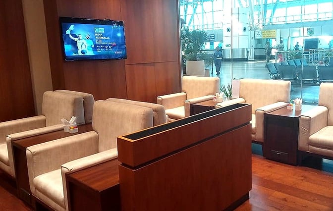 The Bird Lounge at Biju Patnaik International Airport features comfortable seating with individual tables and a television for entertainment.
