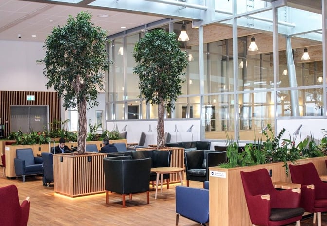 The King Amlet Lounge at Billund Airport features a seating area with armchairs, tables, and indoor plants for relaxation.