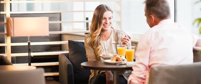 Seating area in Aspire Lounge North at Birmingham Airport features comfortable chairs and tables for dining, with guests enjoying breakfast.