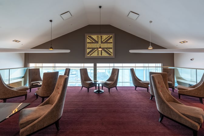 The seating area in No1 Lounge at Birmingham Airport features high-backed chairs and tables with views of the airport tarmac.