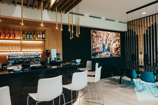 The Prima Vista Lounge at Bologna Airport features a bar with a selection of spirits, coffee machine, and seating area.