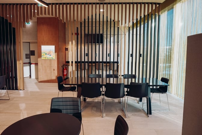 The Prima Vista Lounge at Bologna Airport features a seating area with tables and chairs, separated by vertical slats for privacy.