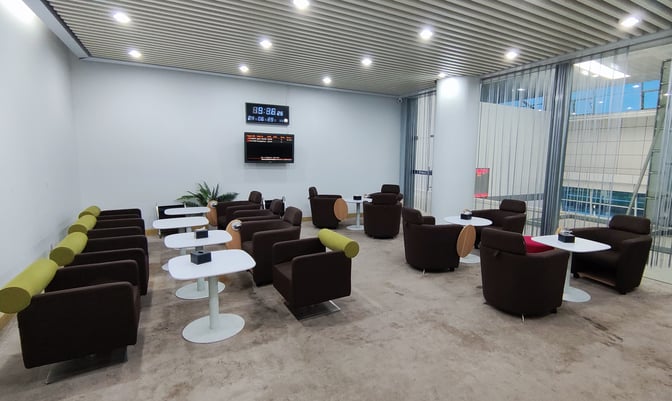 The seating area in Qinhuangdao Beidaihe Airport's First Class Lounge features armchairs and tables with a view of the terminal.
