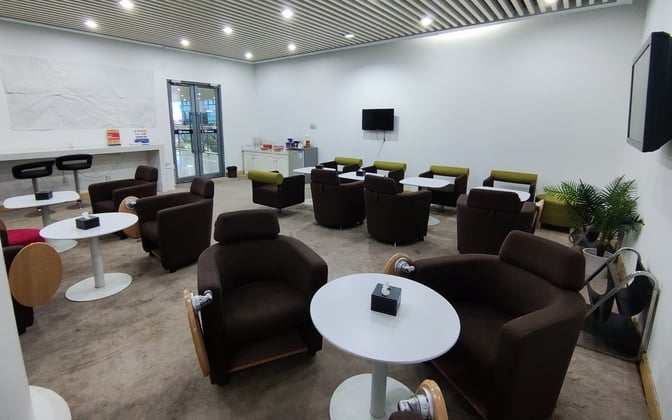 The seating area in Qinhuangdao Beidaihe Airport's First Class Lounge features comfortable chairs and tables, with a small refreshment station nearby.