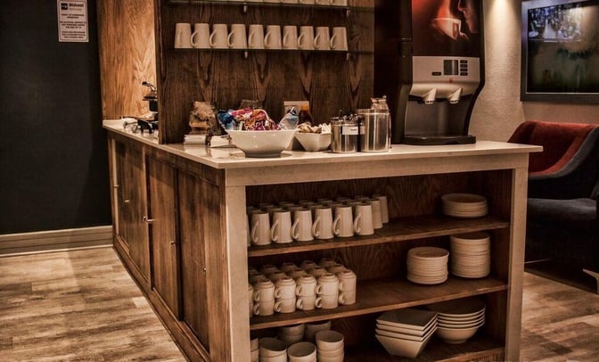 The Bidvest Premier Lounge at Bram Fischer International Airport features a self-serve beverage station with coffee, mugs, and snacks.