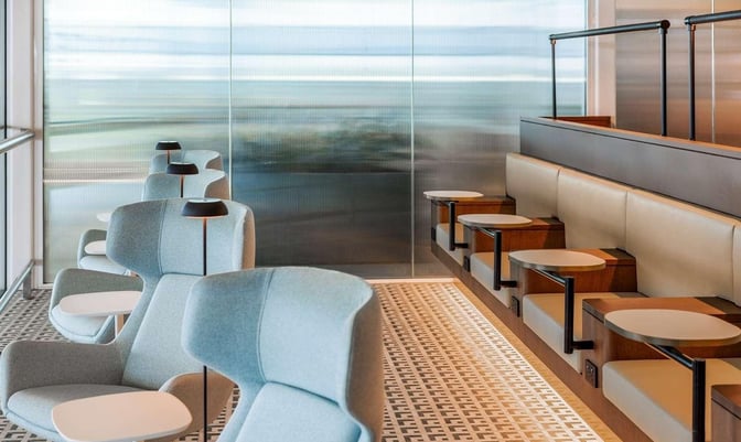 Seating area in Brisbane Airport's Escape Lounge features individual chairs with side tables and a row of booth seating with small tables.