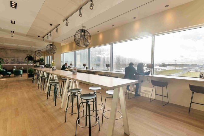 The Diamond Lounge at Brussels Airport features high tables with stools and window seating offering views of the runway.