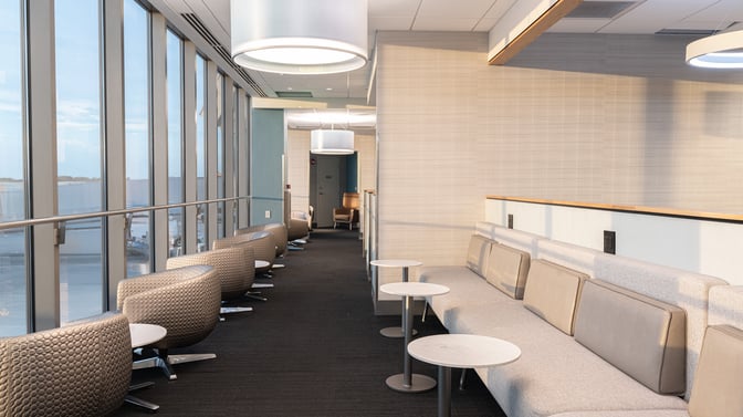 The seating area in The Club BUF at Buffalo Niagara International Airport features lounge chairs and tables with airport views.