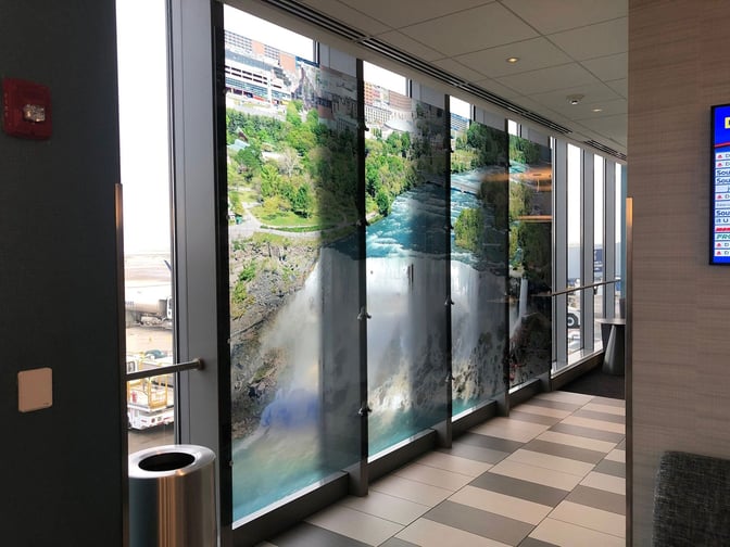 The Club BUF lounge features large windows with scenic wall art and views of the airport tarmac, enhancing the travel experience.