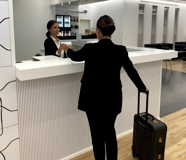 The Prima Vista Lounge reception at Cagliari Elmas Airport features a check-in counter with staff assisting travelers.