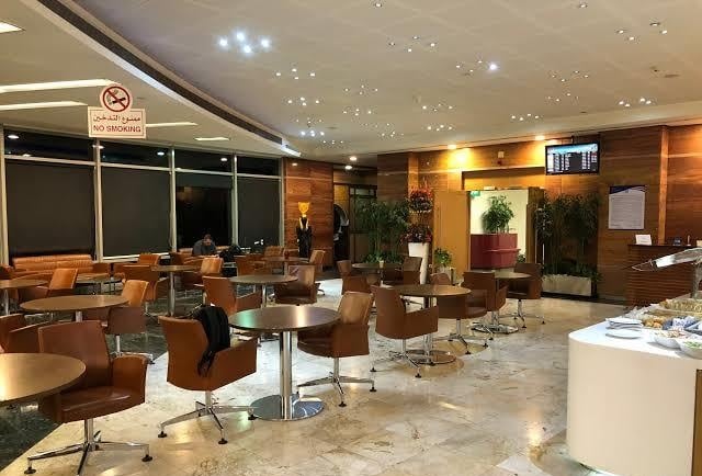 The seating area in the CAC Lounge at Cairo International Airport features round tables and chairs, with a self-serve food station nearby.