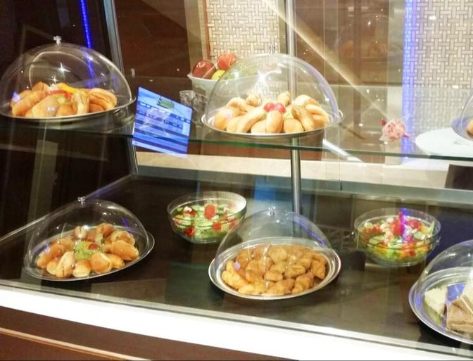 The food display at CAC Lounge features a variety of pastries and salads under clear domes for self-service.
