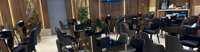 The seating area in the CAC Lounge at Cairo International Airport Terminal 3E features tables and chairs with a nearby self-serve beverage station.