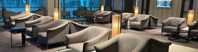 The seating area in the CAC Lounge at Cairo International Airport features comfortable chairs and tables with a view of the terminal.