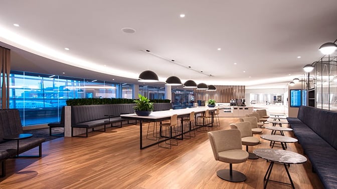 The Elevation Lounge at Calgary International Airport features spacious seating areas with tables, a self-serve food station, and airport views.