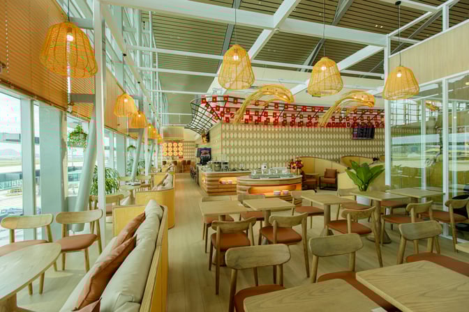 The SH Premium Lounge at Cam Ranh International Airport features a spacious seating area with tables and a self-serve beverage station.