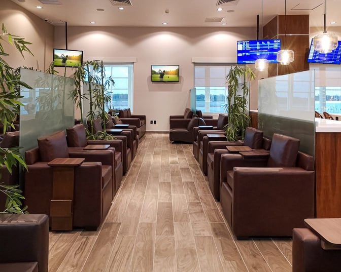The seating area in MERA Business Lounge Terminal 2 features individual armchairs with small tables, TVs, and partial privacy dividers.
