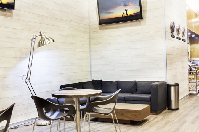 Seating area in MERA Business Lounge, Terminal 3, Cancun Airport, features a sofa, round table, chairs, and a floor lamp.