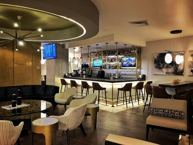 The MERA Business Lounge at Cancun International Airport features a bar with counter seating and a variety of spirits displayed.