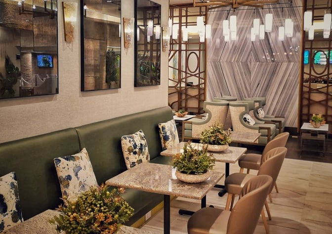 The seating area in MERA Business Lounge Terminal 4 at Cancun International Airport features tables with chairs and decorative plants.