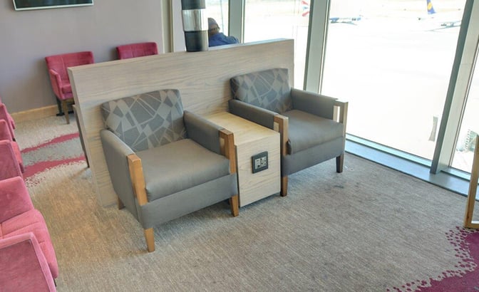Seating area in Bidvest Premier Lounge at Cape Town International Airport features armchairs with a central power outlet and airport views.