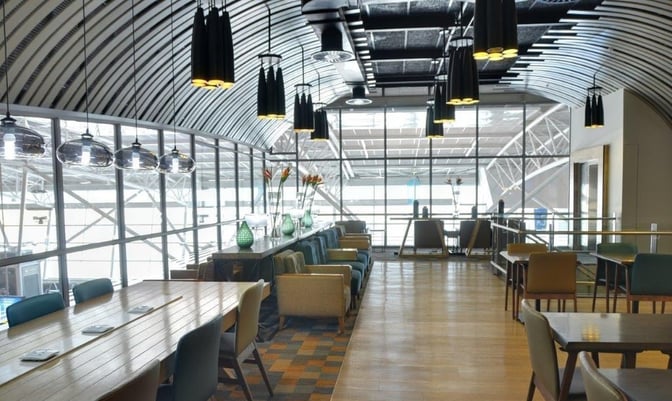 The Bidvest Premier Lounge at Cape Town International Airport features a spacious seating area with tables and chairs overlooking the terminal.