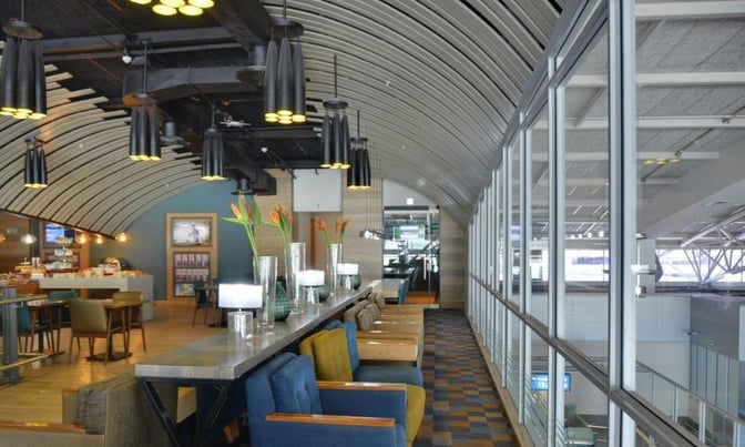 The Bidvest Premier Lounge at Cape Town International Airport features a seating area with tables, chairs, and a view of the terminal.