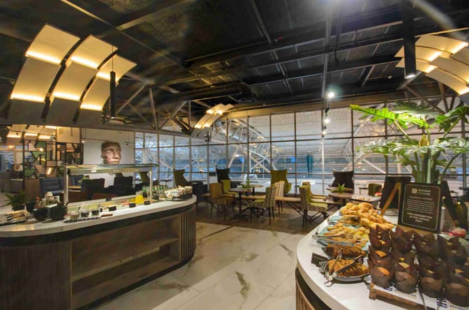 The Bidvest Premier Lounge at Cape Town International Airport features a self-serve food area with pastries and seating overlooking the terminal.