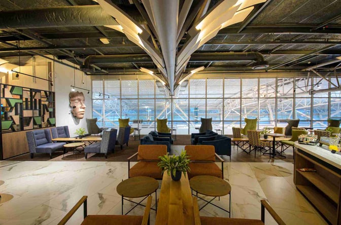 The Bidvest Premier Lounge at Cape Town International Airport features diverse seating areas with tables, offering views of the airport through large windows.