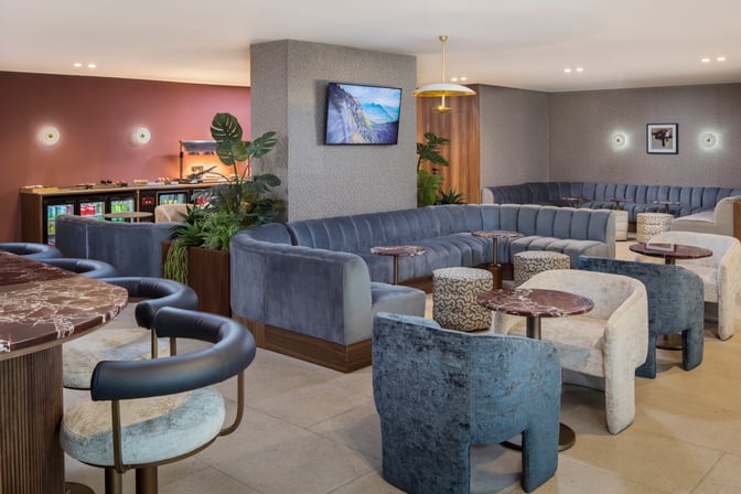 The Casablanca Aspire Lounge Terminal 2 features spacious seating areas with plush chairs and tables, alongside a self-serve beverage station.