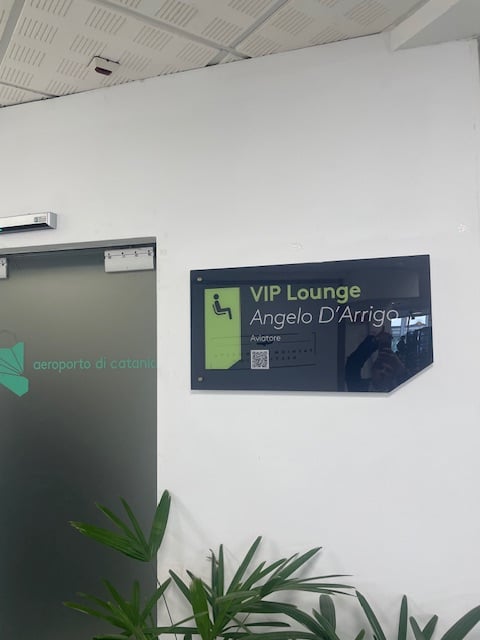 The entrance to the Angelo D'Arrigo VIP Lounge at Catania–Fontanarossa Airport features a sign and a frosted glass door.