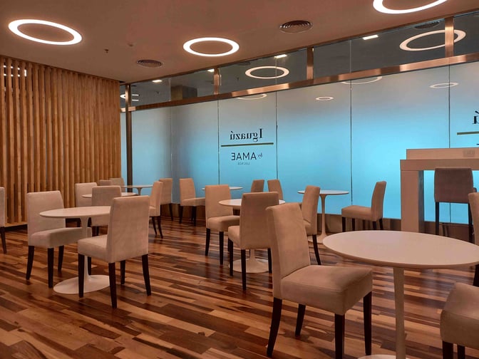 The seating area at Iguazu by AMAE Lounge features round tables and cushioned chairs, providing a comfortable space for travelers.