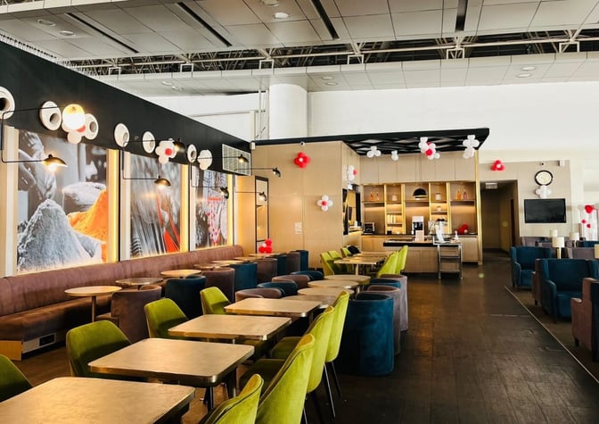 The Primus Lounge at Chandigarh Airport features a seating area with tables and chairs, adjacent to a self-serve beverage station.