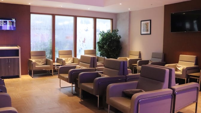 The seating area in Travel Club Lounge A at Chennai International Airport features armchairs, a flight information screen, and a television.