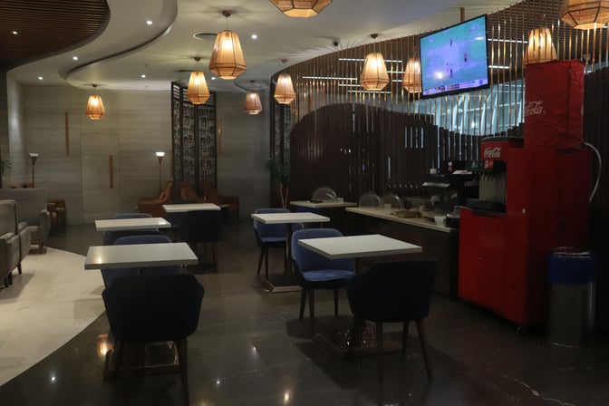 The Travel Club Lounge B at Chennai International Airport features a seating area with tables, chairs, and a beverage station.