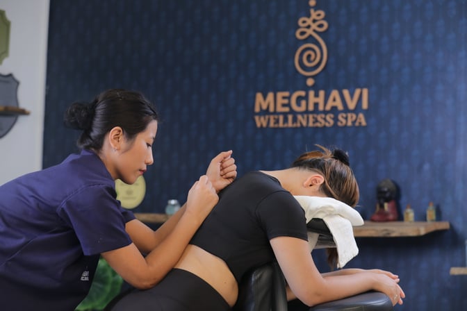 A therapist provides a massage to a client in the Meghavi Wellness Spa, featuring a treatment chair and relaxing environment.