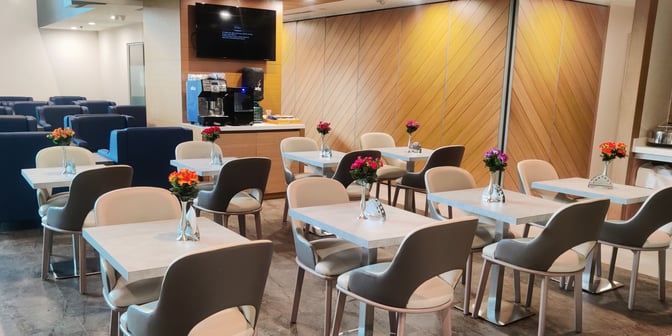 The Aviserv Lounge at Chhatrapati Shivaji International Airport features a seating area with tables, chairs, and a self-serve coffee station.