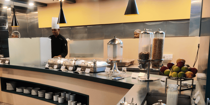 The food service area at Aviserv Lounge features buffet-style chafing dishes, cereal dispensers, and fresh fruit for travelers.