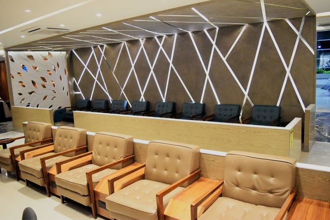 The seating area in the Travel Club Lounge at Chhatrapati Shivaji International Airport features cushioned chairs and a partitioned wall design.