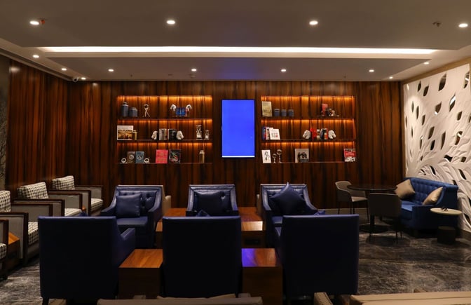 The seating area in the Travel Club Lounge at Chhatrapati Shivaji International Airport features comfortable chairs and decorative shelving.