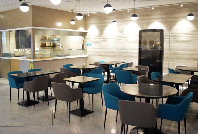 The seating area in the Travel Club Lounge at Chhatrapati Shivaji International Airport features tables and chairs near a self-serve food counter.