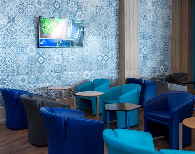 The seating area in Bangkok Airways Boutique Lounge at Chiang Mai International Airport features comfortable chairs and small tables with a wall-mounted TV.